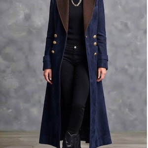 May include: A long navy blue coat featuring a brown textured lapel, double-breasted gold buttons, and long sleeves. The coat is worn over a black turtleneck sweater, black trousers, and black boots, with a silver chain necklace around the neck.