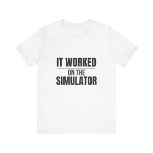 Könnte beinhalten: Ein weißes kurzärmeliges T-Shirt mit dem schwarzen Text "IT WORKED ON THE SIMULATOR", der in einer fetten, serifenlosen Schrift mittig auf der Brust aufgedruckt ist. Das Kleidungsstück hat einen Rundhalsausschnitt und einen geraden Schnitt.