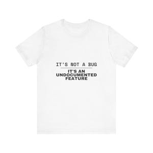 May include: A white short-sleeved t-shirt featuring black text centred on the chest that reads: IT'S NOT A BUG, IT'S AN UNDOCUMENTED FEATURE. The shirt has a crew neckline and a standard fit, constructed from a plain white fabric with dark lettering.