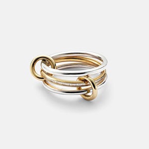 May include: A multi-band ring featuring a combination of polished silver-tone and gold-tone metal bands. The design includes two smaller gold-tone rings that interlock with the main stack, which consists of smooth and baguette-cut stone bands.