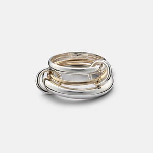 May include: A multi-band ring featuring a combination of polished silver-tone and gold-tone metal bands. The design consists of several interlocking circular bands of varying thicknesses that are connected to form a single cohesive jewelry piece.