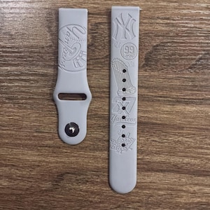 May include: A light grey silicone watch strap featuring embossed New York Yankees baseball graphics. The shorter strap includes a metal pin closure, while the longer strap displays various team logos, the text Yankees, and Bronx Bombers.