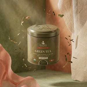 May include: A cylindrical olive green metal tea tin labeled Cecilia Terra Organic Rwandan Green Tea. The label displays the text Net Wt. 3.5 oz (100 g) and Loose leaf tea. Dried tea leaves float in the air around the container.