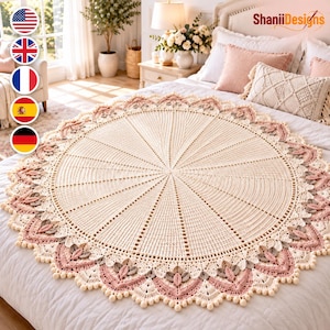 May include: A large, circular, cream-colored crochet blanket featuring a radial pattern with intricate stitching. The border is decorated with layered, petal-like motifs in shades of dusty pink and soft gray, finished with small, round pom-pom edges.