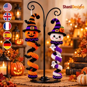 May include: Two crocheted Halloween ornaments hanging from a black metal stand. One is an orange pumpkin with a striped hat and black bats, the other is a white ghost with a purple striped hat, a small pumpkin, and tiny white ghost accents.