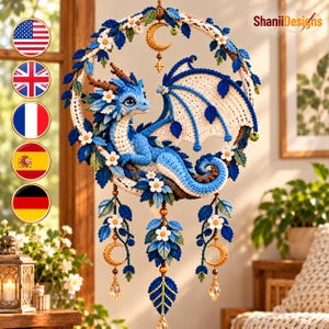 May include: A circular crochet wall hanging featuring a blue dragon with white wings, surrounded by blue leaves and white flowers. A gold crescent moon charm hangs from the top, with three dangling strands of leaves, flowers, and gold moons.