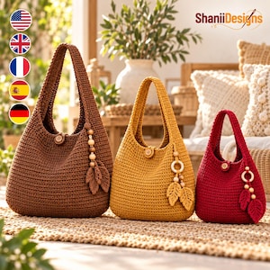 May include: Three handmade crochet hobo bags in brown, mustard yellow, and deep red. Each bag features a single shoulder strap, a central wooden button closure, and a decorative hanging charm consisting of wooden beads and two crocheted leaves.