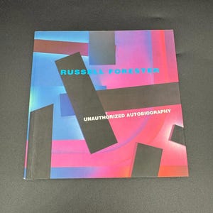 May include: A square book titled Russell Forester Unauthorized Autobiography. The cover features a vibrant gradient background of blue, purple, and pink, overlaid with several solid black rectangular shapes arranged in various orientations.