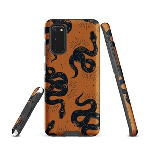 Pode incluir: Uma capa de smartphone com fundo laranja queimado e um padrão repetitivo de cobras azul-marinho escuro. As cobras são decoradas com motivos celestiais brancos, incluindo estrelas, raios de sol e constelações. Exibida a partir de três ângulos.