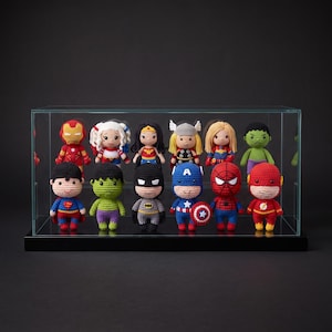 May include: A collection of twelve small, crocheted superhero and villain dolls displayed inside a clear glass rectangular case with a black base. The figures feature detailed yarn stitching, vibrant colours, and recognisable character costumes.