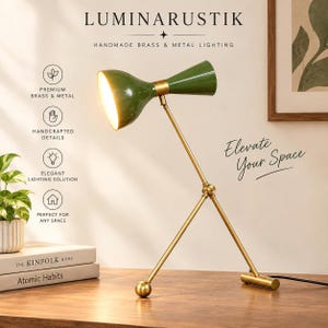 Könnte beinhalten: Eine Schreibtischlampe mit einem olivgrünen Doppelkegel-Lampenschirm und einem Metallgestell in Messingoptik. Die Lampe verfügt über einen verstellbaren Arm mit einem zentralen Gelenk und einen Stativfuß. Der Text umfasst LUMINARUSTIK und Elevate Your Space.