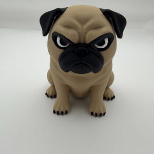 May include: A tan pug figurine with a black muzzle, black ears, and black paws. The dog has a textured, wrinkled face with white eyes and black pupils, sitting in an upright position with a stern, focused expression on its face.