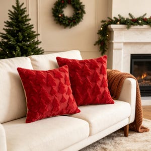 May include: Two square throw pillows in a vibrant red color, featuring a raised, textured pattern of repeating Christmas tree shapes across the front surface. The pillows are made of a soft, plush material and have a consistent, solid red hue.