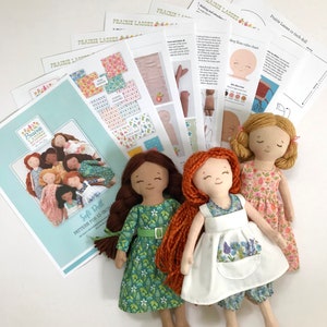May include: A set of three 12-inch soft dolls with long, red hair. The dolls are wearing different dresses: one green, one white, and one pink. The dolls are accompanied by a set of instructions for making a soft doll.
