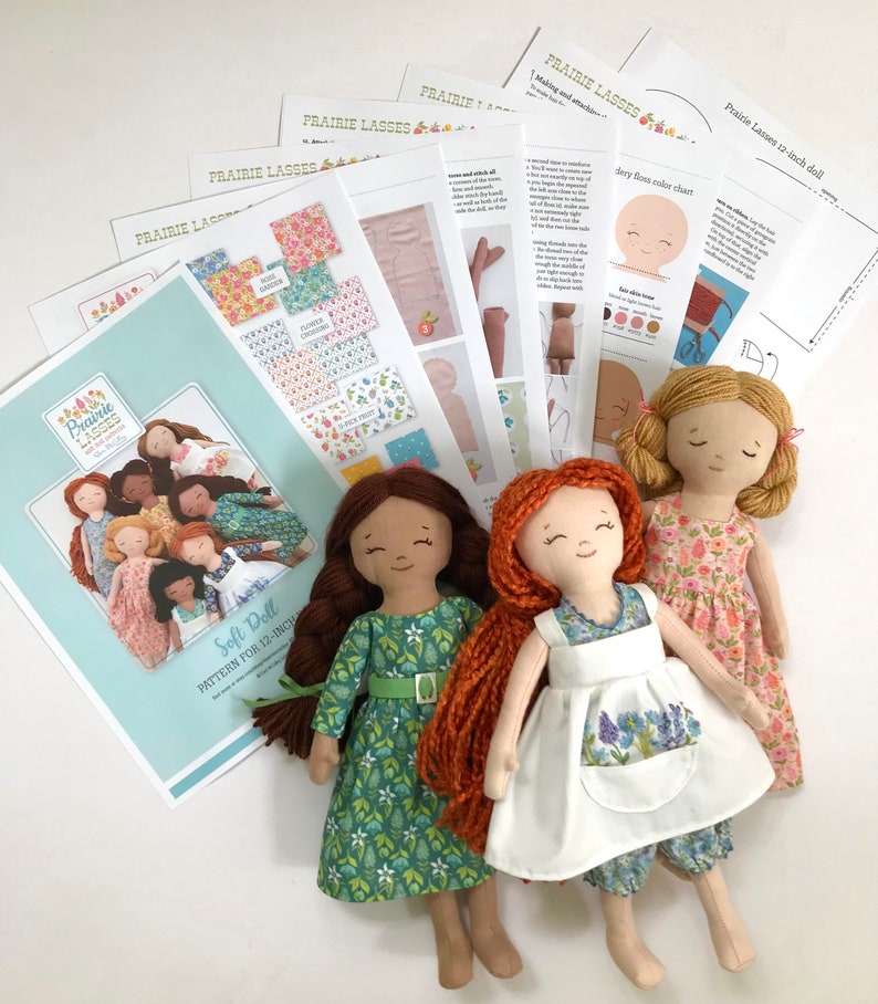 May include: A set of three 12-inch soft dolls with long, red hair. The dolls are wearing different dresses: one green, one white, and one pink. The dolls are accompanied by a set of instructions for making a soft doll.