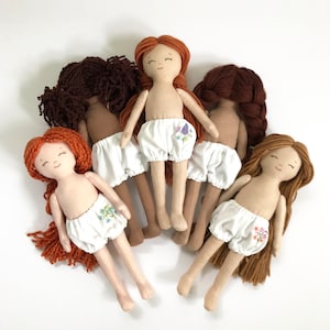 May include: Five handmade cloth dolls with embroidered floral details on their white bloomers. The dolls have yarn hair in various shades of brown and red.