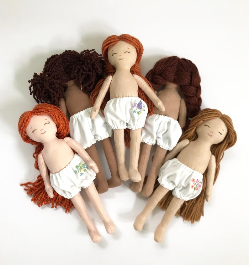 May include: Five handmade cloth dolls with embroidered floral details on their white bloomers. The dolls have yarn hair in various shades of brown and red.