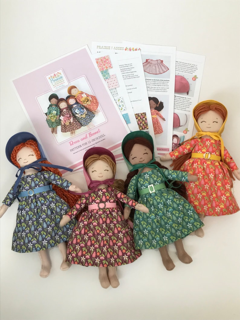 May include: Four 12-inch dolls wearing different floral print dresses and bonnets. The dolls have brown hair and are wearing brown shoes. The dolls are arranged in a circle on a white surface. The image also includes a printed pattern for a dress and bonnet.
