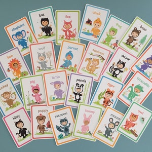 May include: A set of 24 colorful flashcards featuring various animals dressed in costumes. Each card has a different animal name printed on it, such as elephant, bat, fox, chick, frog, bear, lion, wolf, parrot, squirrel, skunk, hippo, crocodile, monkey, pig, lamb, kitty, puppy, raccoon, panda, tiger, bunny, mouse, and owl.