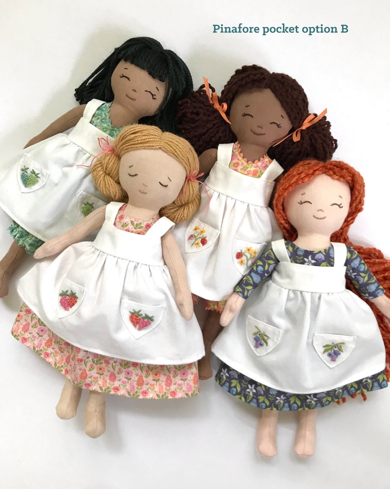 May include: Four handmade dolls wearing white pinafores with embroidered pockets. The dolls have different hair colours and skin tones. The pinafores have different floral patterns on the bottom.