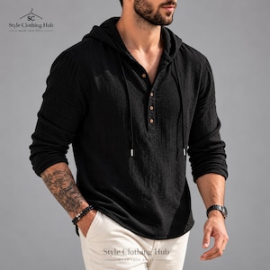 May include: A black long-sleeve hooded shirt featuring a textured fabric, a four-button placket with light brown buttons, and matching black drawstrings. The garment is paired with light-colored trousers and displays the Style Clothing Hub logo.
