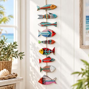 Pode incluir: Um adorno de parede vertical com nove figuras de peixes de madeira penduradas numa corda. Cada peixe é pintado em várias cores, incluindo vermelho, azul, amarelo e verde com um acabamento desgastado, dispostos numa única coluna.