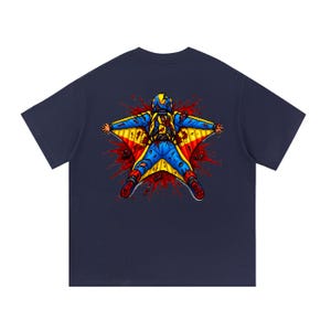 Puede incluir: Una camiseta azul marino con un gráfico en la espalda de una persona con un traje de alas azul y amarillo. La figura aparece en posición extendida sobre un fondo de salpicaduras rojas, con manchas rojas visibles en el traje y el casco.