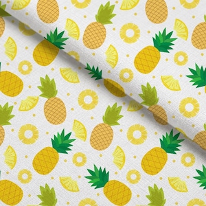 Könnte beinhalten: Ein weißer Stoff mit einem sich wiederholenden Muster aus gelben Ananas mit grünen Blättern, gelben Ananasringen und gelben Ananasstücken, durchsetzt mit kleinen gelben Punkten auf der gesamten Oberfläche des Textils.