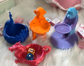 以下が含まれることがあります： 3Dプリントされた4つの装飾用ボウルとトレイのセット。青いクジャク、葉の形のトレイを持つオレンジ色のサル、円形のトレイを持つ紫色のサル、そして2つのサイコロが入った赤いドラゴンの形のボウルが含まれています。