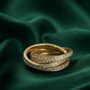 May include: A gold rolling ring composed of three interlocking bands, each featuring a continuous pavé setting of small, clear, round-cut stones that catch the light, creating a shimmering effect across the entire surface of the jewelry piece.