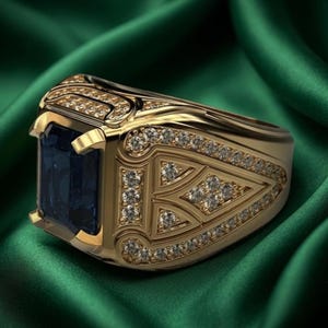Pode incluir: Um anel de ouro com uma grande pedra preciosa retangular azul-escura no centro. A banda &eacute; larga e feita de ouro, decorada com numerosas pedras pequenas, claras e de corte redondo dispostas em padr&otilde;es geom&eacute;tricos nas laterais e no topo.