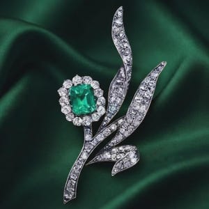 Op de afbeelding: Een bloemvormige broche van zilverkleurig metaal, met een centrale rechthoekige smaragd omringd door een halo van kleine heldere stenen. De steel en bladeren zijn ingelegd met talloze kleine, fonkelende heldere stenen.
