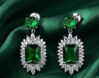 May include: A pair of silver-toned drop earrings featuring a large, rectangular, emerald-green center stone surrounded by a halo of small, clear, marquise-cut stones, topped with a single, round, emerald-green stone set in a silver-toned base.