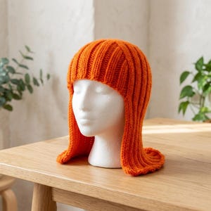 May include: A bright orange knitted hat with a ribbed texture that covers the crown and extends down the sides to frame the face. The headwear features a vertical knit pattern throughout, creating a consistent look from the top to the edges.