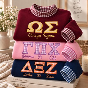 Peut inclure: Une pile de trois sweat-shirts à manches longues avec des cols montants. Le haut est bordeaux avec des lettres grecques Omega Sigma en vichy jaune. Le milieu est rose avec des lettres grecques Gamma Pi Chi en vichy violet. Le bas est bleu marine avec des lettres grecques Delta Xi Zeta en vichy orange.