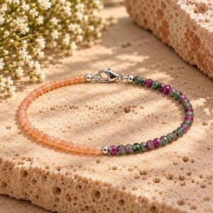 May include: A delicate bracelet featuring a strand of faceted peach-coloured sunstone beads on one side and a strand of faceted green and magenta ruby zoisite beads on the other, connected by a silver-toned lobster claw clasp and small metal beads.