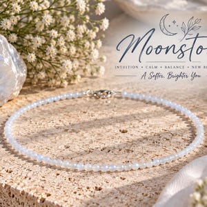 Puede incluir: Un delicado collar de cuentas con pequeñas cuentas de piedra lunar azul claro translúcidas dispuestas en un patrón circular. El texto "Moonstone INTUITION + CALM + BALANCE + NEW BEGINNINGS A Softer, Brighter You" es visible en la esquina superior derecha.