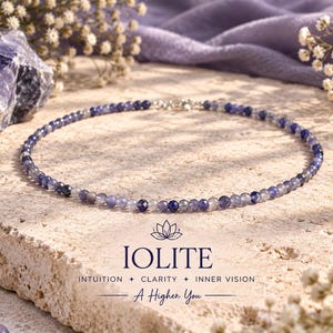 May include: A beaded necklace featuring small, faceted, translucent blue and violet iolite gemstones arranged in a circular pattern. The text below the necklace reads IOLITE, INTUITION + CLARITY + INNER VISION, and A Higher You.
