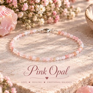 Può includere: Un braccialetto delicato composto da piccole perle di opale rosa sfaccettate con una chiusura in metallo color argento. Il testo "Pink Opal" è stampato in corsivo sopra le parole "LOVE HEALING EMOTIONAL BALANCE" con piccole icone a cuore.