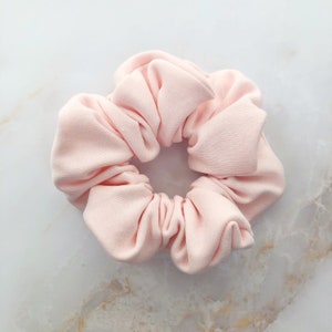 May include: A soft, pink scrunchie made of fabric. It is a hair accessory for tying up hair.