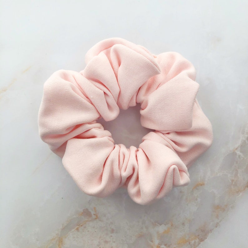 May include: A soft, pink scrunchie made of fabric. It is a hair accessory for tying up hair.