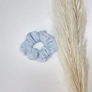 May include: A light blue scrunchie made of soft fabric. The scrunchie is in the shape of a circle and has a gathered look.