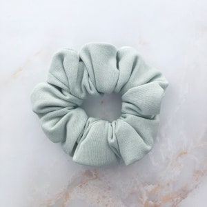 May include: A light green scrunchie made of soft fabric. The scrunchie is in the shape of a flower.