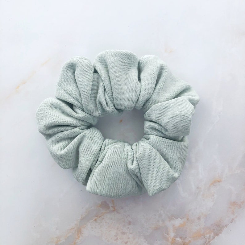 May include: A light green scrunchie made of soft fabric. The scrunchie is in the shape of a flower.