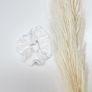 May include: A white fabric scrunchie for hair. The scrunchie is made of soft, smooth fabric and is a simple, elegant design.