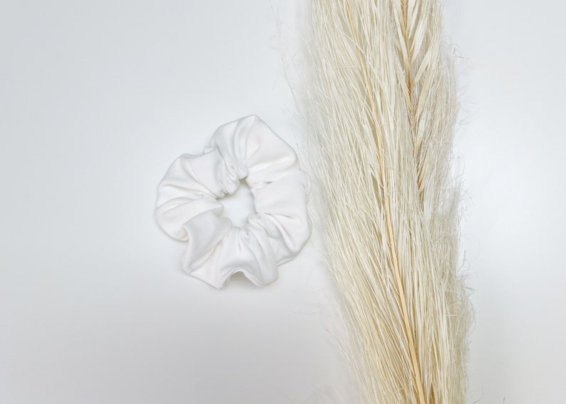 May include: A white fabric scrunchie for hair. The scrunchie is made of soft, smooth fabric and is a simple, elegant design.