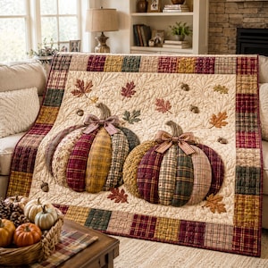 Op de afbeelding: Een rechthoekige quilt met twee grote, driedimensionale stoffen pompoenen in rood, goud en groen geruite patronen. De crèmekleurige achtergrond is doorgestikt met bladpatronen en de rand bestaat uit een veelkleurige geruite stof.