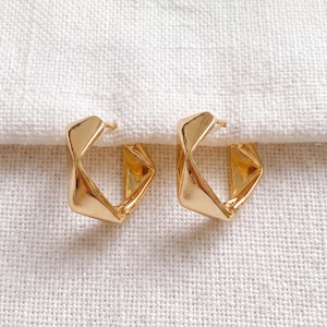 May include: A pair of gold-toned hoop earrings featuring a geometric, angular, and faceted design. The earrings have a polished, reflective surface and a thick, open-frame construction that creates a distinct, multi-sided shape.