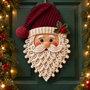 May include: A crocheted Santa Claus wall hanging featuring a deep red hat with a pom-pom, a beige face with black eyes, pink cheeks, and a textured white beard made of layered crochet petals. A small sprig of green holly leaves and red berries is attached.