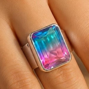 May include: A silver-toned ring featuring a large, rectangular, faceted gemstone with a gradient color transition from vibrant blue at the top to a bright pink at the bottom, set in a smooth, polished metal band.